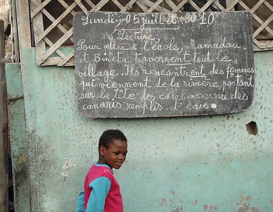 Photo of a Senegalese child standing near a chalkboard.